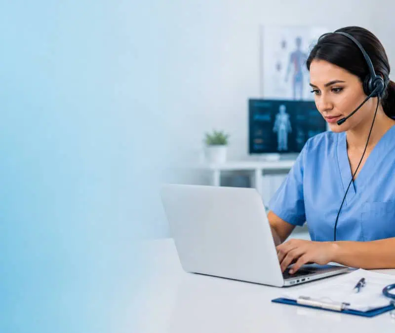 Healthcare professional in blue scrubs wearing a headset and typing on a laptop, with a soft blue gradient on the left and medical office equipment on the desk.