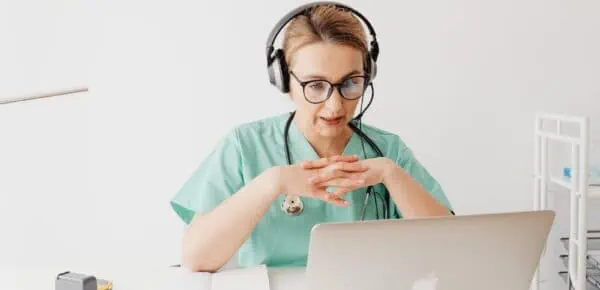 Woman in Scrub Suit Sitting In Front of a Laptop on a Video Call for a transcription overflow article