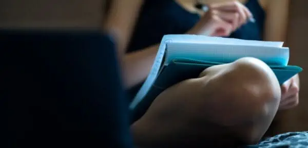 person holding blue and white pad while writing their dissertation.