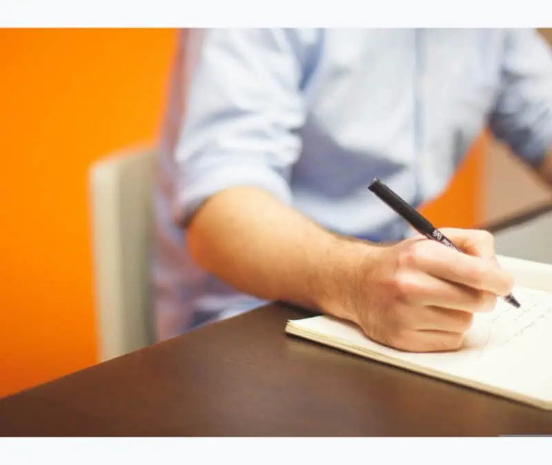 a person in his desk, writing notes in fron of his laptop