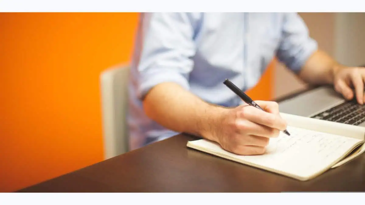 a person in his desk, writing notes in fron of his laptop