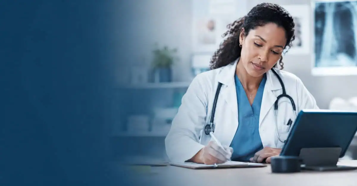 A physician reviews patient information while writing clinical notes beside a tablet in a modern medical office, representing AI-assisted medical documentation and clinical recordkeeping.